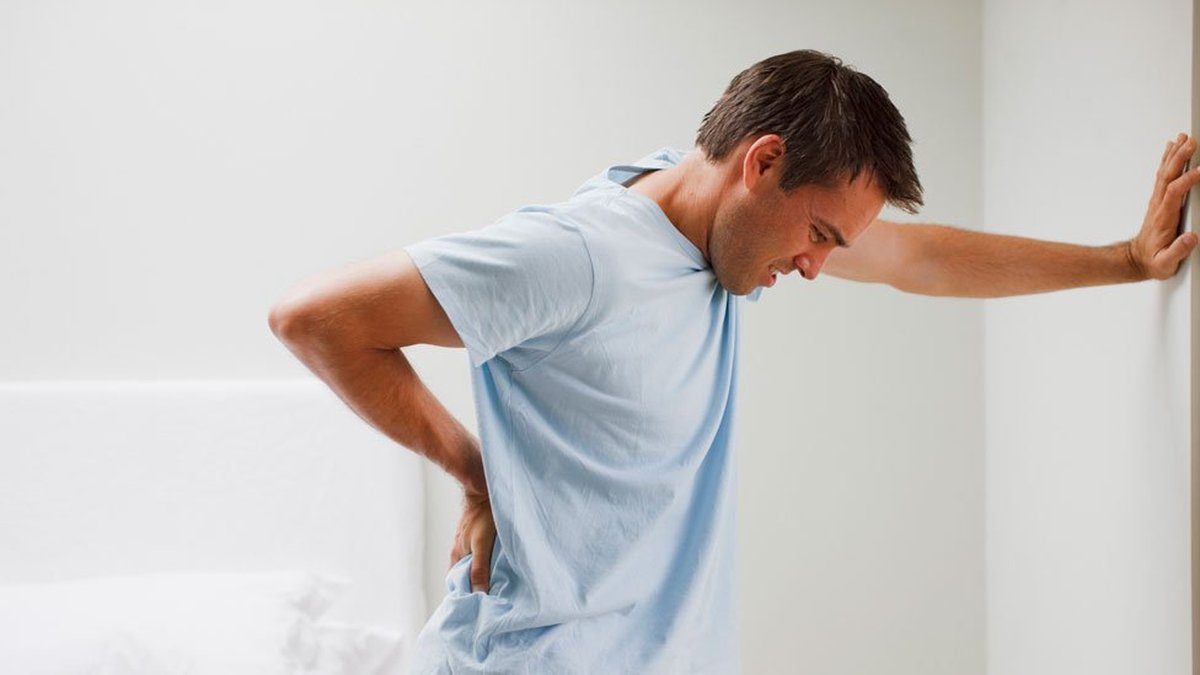 Hombre sufriendo dolor lumbar agudo apoyándose en la pared, una de las patologías que tratamos en MEFIR Barcelona
